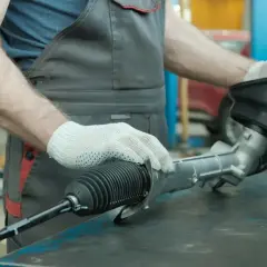 Mechanik w rękawiczkach trzyma uszkodzoną maglownicę samochodową.