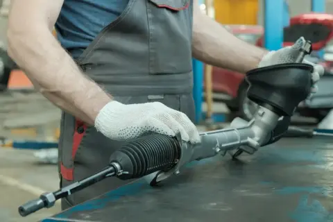 Mechanik w rękawiczkach trzyma uszkodzoną maglownicę samochodową.