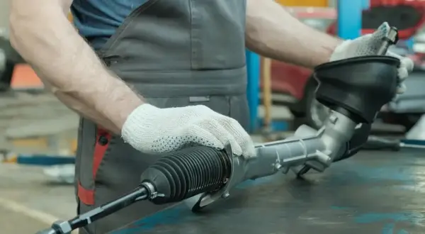 Mechanik w rękawiczkach trzyma uszkodzoną maglownicę samochodową.